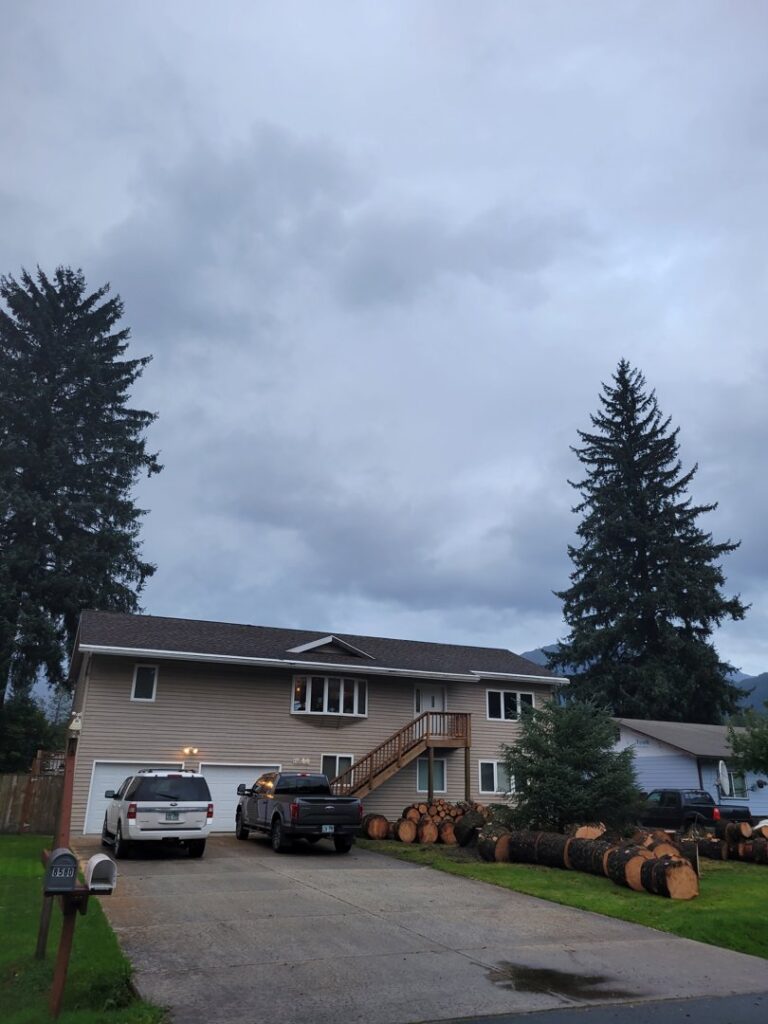 Large felled logs stacked in a residential driveway, indicating recent tree removal by Everybody's Tree Service in Juneau, AK.