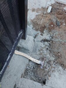 A metal fence post installation in progress with a hammer and string line, provided by Handyman Services of Albuquerque in Albuquerque, NM.