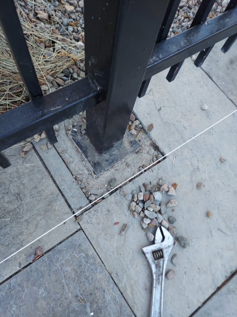 Close-up of a metal fence post being repaired on a patio with a wrench, demonstrating services from Handyman Services of Albuquerque in Albuquerque, NM.