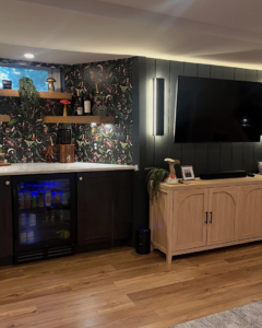 A beautifully finished basement entertainment area with a built-in bar, mini-fridge, and mounted TV by Chesapeake Premier Remodeling in Baltimore, MD