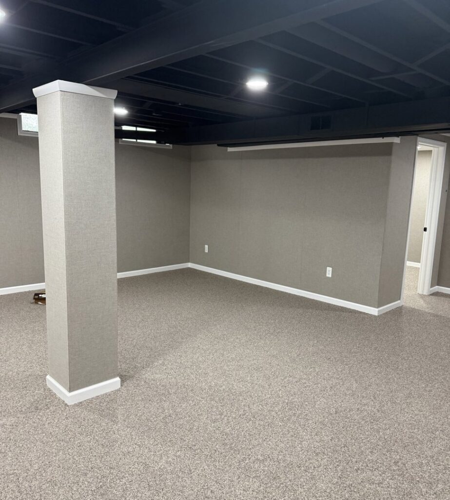 A finished basement room with new carpeting, a wrapped column, and a dark ceiling by Impressive Basements in Westland, MI.