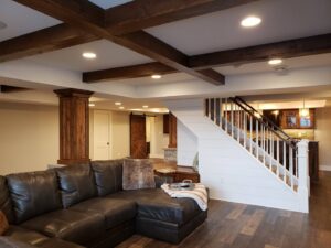 A newly finished basement living area featuring exposed wooden beams and a modern staircase by Kahle Builders, LLC in Waukesha, WI.