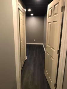 A renovated basement hallway featuring dark wood-look flooring and white doors by M Zimmer Construction LLC in Rochester, NY.