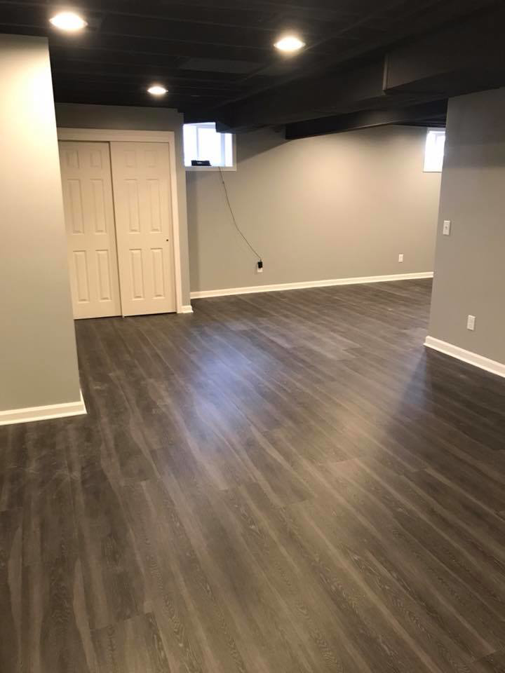 A spacious finished basement living area with dark flooring and light gray walls by M Zimmer Construction LLC in Rochester, NY.