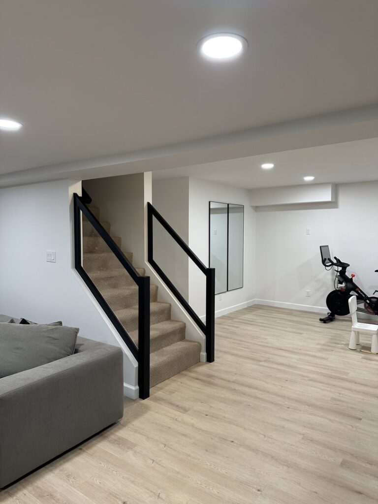 A newly finished basement living area with modern stairs, wood-look flooring, and recessed lighting by Westrick Homes in St. Louis, MO.