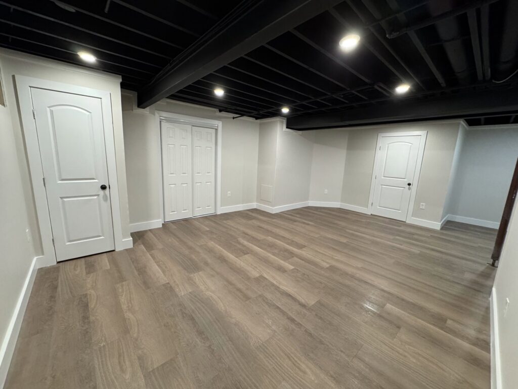 A finished basement room with new flooring, painted ceiling, and recessed lighting by Gateway Home Services KC LLC in Kansas City, MO.