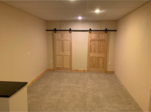A newly remodeled basement room featuring new carpet and stylish barn doors installed by Berling Remodeling llc in Highland Heights, KY.