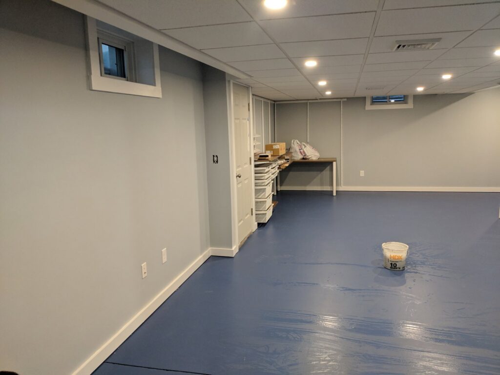 A newly finished basement renovation with painted walls and a blue epoxy floor by BizMick Construction in Coventry, RI.
