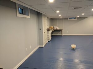 A newly finished basement renovation with painted walls and a blue epoxy floor by BizMick Construction in Coventry, RI.