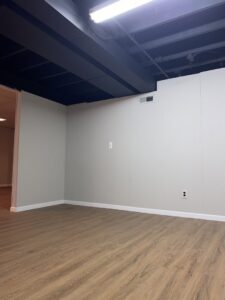 A newly finished basement room with painted walls, wood-look flooring, and an exposed ceiling by RT Property Services in Allendale, MI