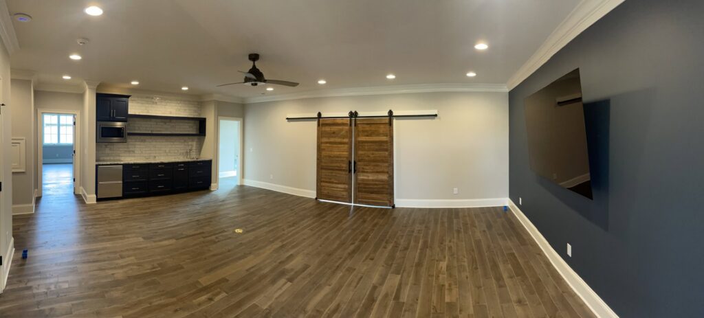 A newly finished basement with a wet bar, barn doors, and wood flooring by Specialty Service Group in Knoxville, TN.