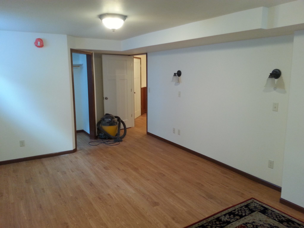 A newly renovated basement room with wood laminate flooring and white walls, completed by Work Horse Contracting in West Fargo, ND.