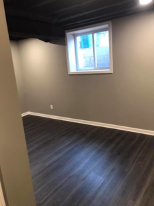 A newly finished basement room with dark wood-look flooring and light gray walls by M Zimmer Construction LLC in Rochester, NY.
