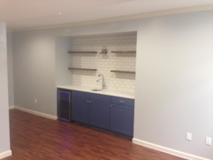 A finished basement area featuring a wet bar with subway tile, blue cabinets, and new flooring by J Development in Pittsburgh, PA.