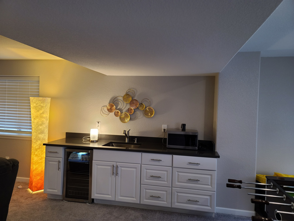 A newly installed wet bar in a finished basement by QCON LLC in Aurora, CO, featuring cabinets, sink, and mini-fridge.