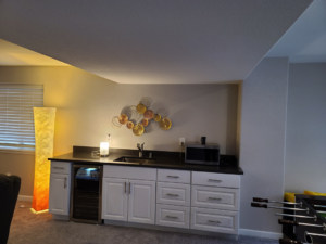 A newly installed wet bar in a finished basement by QCON LLC in Aurora, CO, featuring cabinets, sink, and mini-fridge.