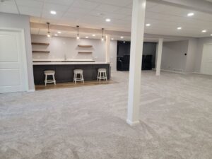 Spacious finished basement featuring a wooden bar, white support columns, and carpet by Pioneer Basement Solutions in Canton, OH.