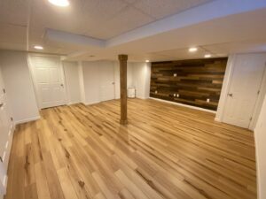A newly finished basement featuring hardwood floors, recessed lighting, and a modern wood accent wall by Rock Solid Construction in Rochester, NY