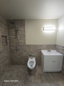 A finished bathroom remodel showcasing a new vanity, toilet, and tiled shower area by Torres Services in Anchorage, AK.