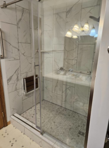 A finished bathroom shower remodel featuring a glass door, fold-down seat, and grab bar by Tim's handyman service in Cherry Hill, NJ.