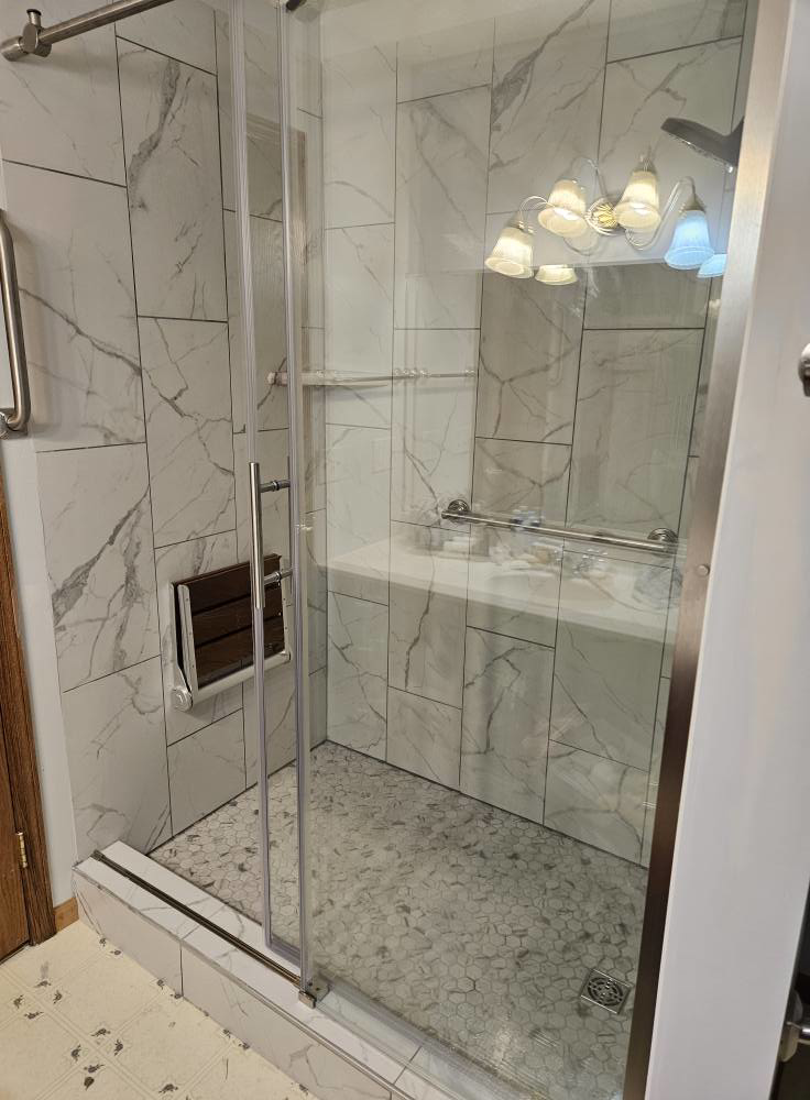 A finished bathroom shower remodel featuring a glass door, fold-down seat, and grab bar by Tim's handyman service in Cherry Hill, NJ.