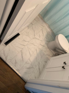 A completed bathroom tile installation with a white toilet and floor vent by Humphrey's Helping Hands in Clarksville, TN.