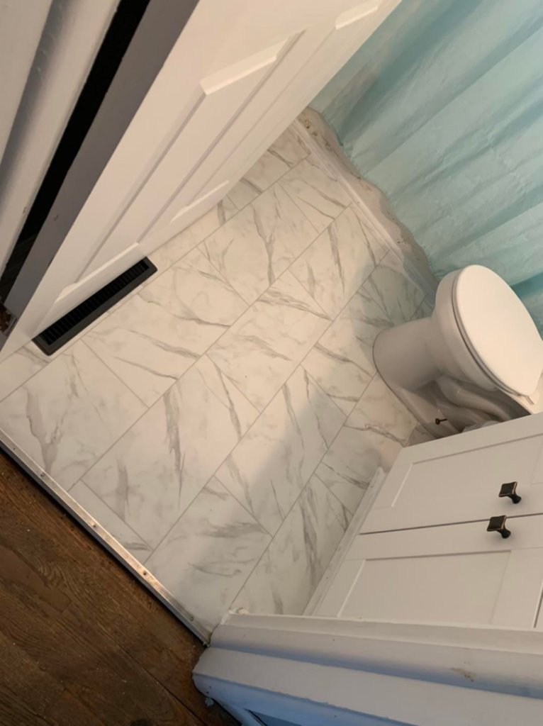 A completed bathroom tile installation with a white toilet and floor vent by Humphrey's Helping Hands in Clarksville, TN.