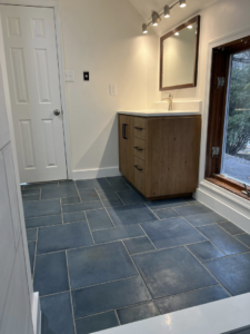 A finished bathroom renovation showcasing a modern wooden vanity, mirror, and dark blue floor tiles by Great Home Construction LLC in Annapolis, MD.