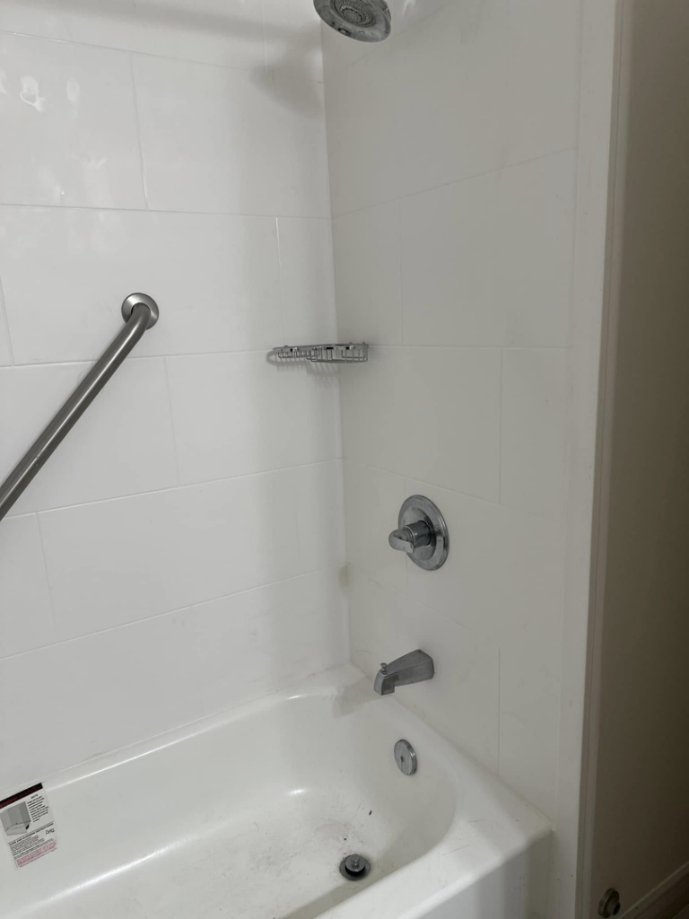 A newly installed bathtub and shower with white tiles and a grab bar by Jay's Construction in Cincinnati, OH.