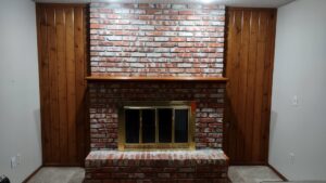 A finished brick fireplace with wood paneling and a mantel by Gateway Home Services KC LLC in Kansas City, MO.