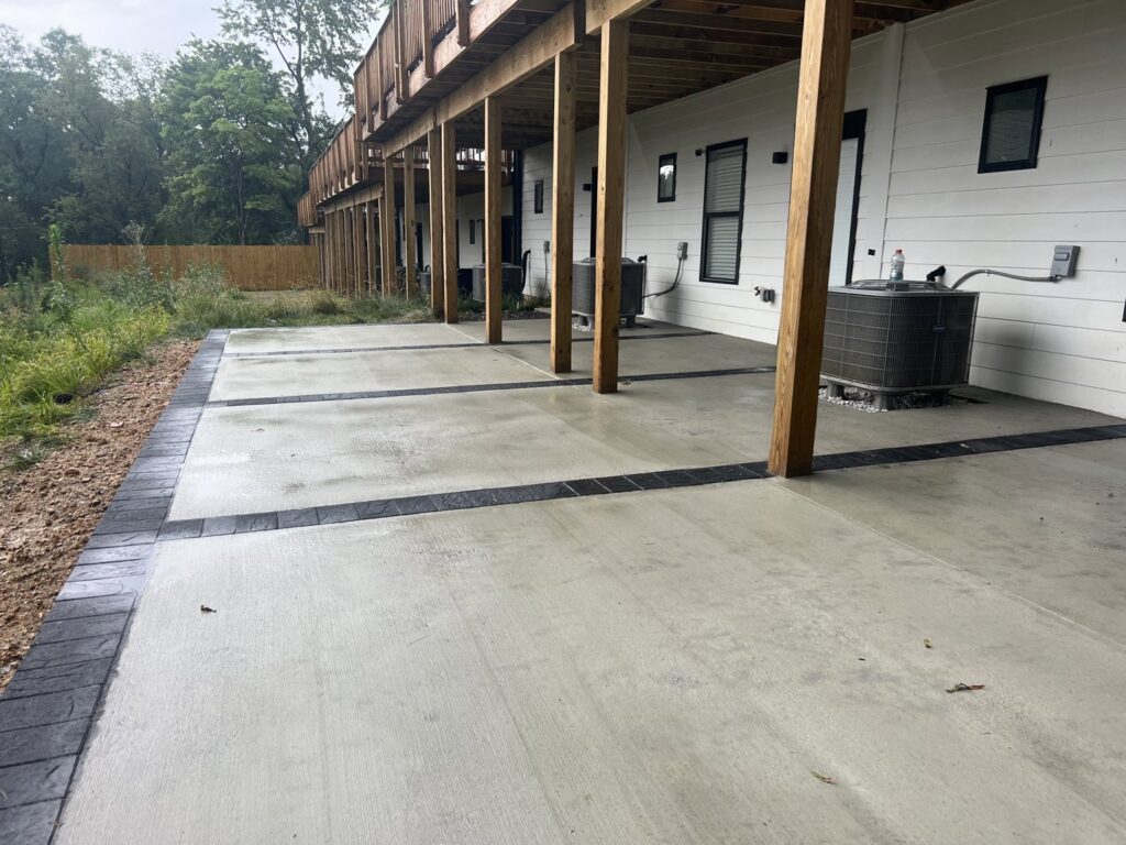 A finished concrete patio with decorative black borders under a deck, installed by Landscape By Today in Bowie, MD.