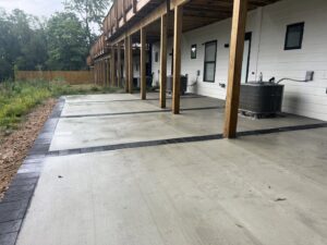 A finished concrete patio with decorative black borders under a deck, installed by Landscape By Today in Bowie, MD.