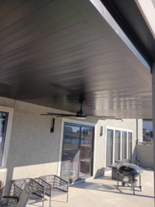 A modern finished dark patio ceiling with an installed ceiling fan by Dry Deck Ceilings KC in Kansas City, KS.