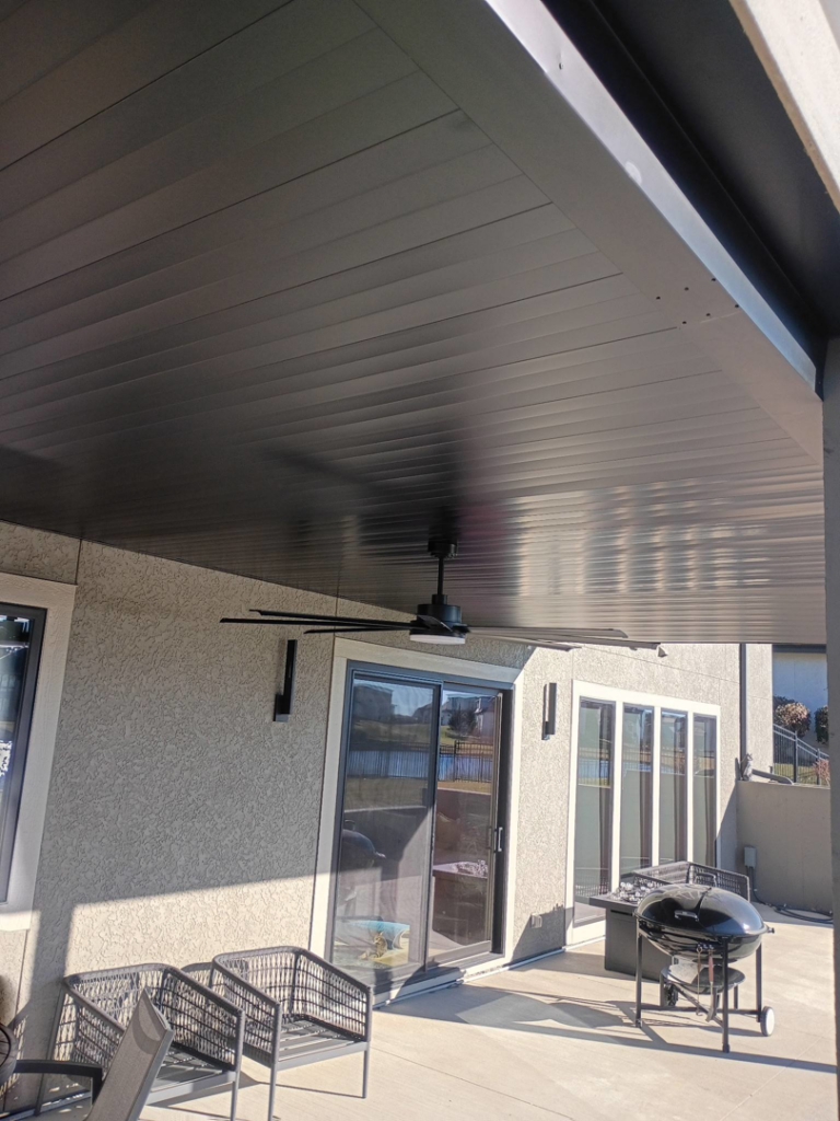 A modern finished dark patio ceiling with an installed ceiling fan by Dry Deck Ceilings KC in Kansas City, KS.