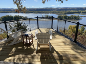 A beautiful finished deck with modern cable railings and Adirondack chairs, offering a scenic river view, built by Building Arts by Jimmy Z in Cassville, WI.