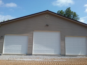 The finished exterior of a garage building with siding and three white garage doors by The House Doctor in Hopkinsville, KY.