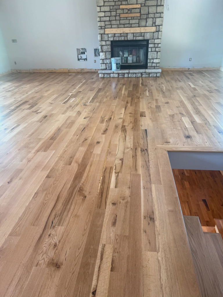 A spacious room with a beautifully finished hardwood floor, stone fireplace, and stairs by Cordell Hardwood Flooring in Lexington, KY.
