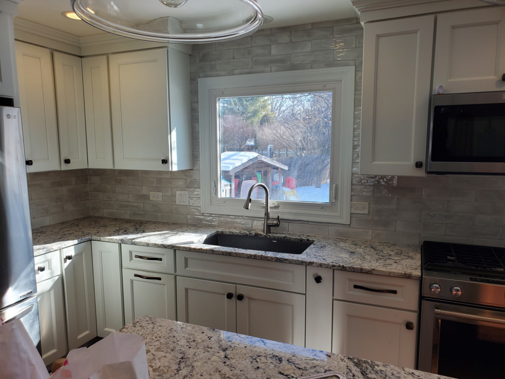 A finished kitchen showcasing white cabinets, granite countertops, and a tiled backsplash by Tile Works inc in Naperville, IL.