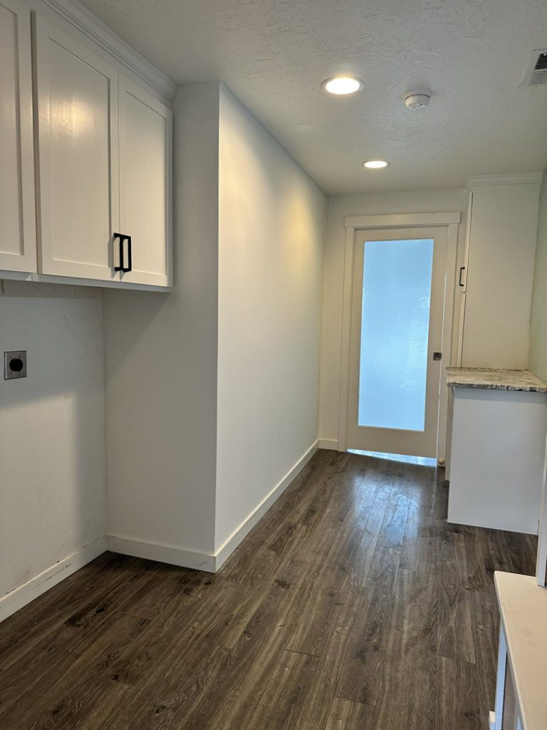 A newly finished laundry room featuring white cabinets, dark flooring, and a frosted glass door installed by Valleys Finest Custom Finishes LLC in Salem, OR.