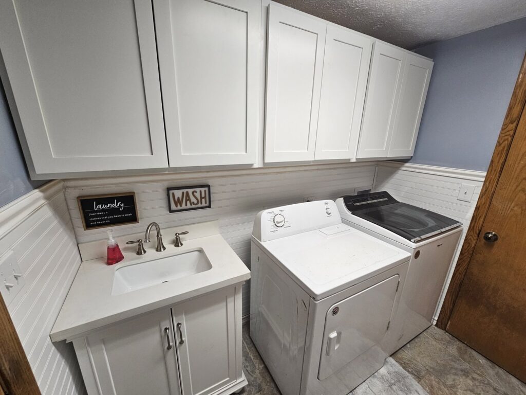 A newly finished laundry room renovation with white cabinets, a utility sink, and wainscoting by Ben Nye The Fix-It Guy in Erie, PA.
