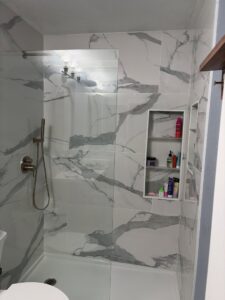 A finished modern shower remodel featuring marble-look tiles and a glass door by Castillejo Handyman Services in San Diego, CA