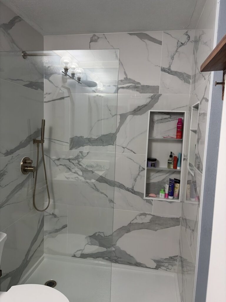 A finished modern shower remodel featuring marble-look tiles and a glass door by Castillejo Handyman Services in San Diego, CA