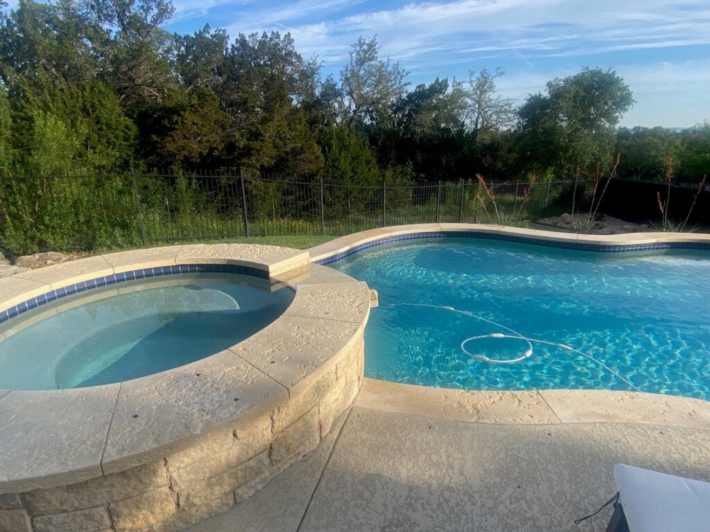 A finished swimming pool and hot tub area with clear water by 5 Daughters Total Outdoors in Austin, TX.