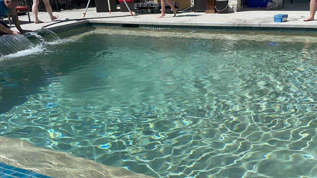A finished swimming pool and patio area with clear water by 5 Daughters Total Outdoors in Austin, TX.
