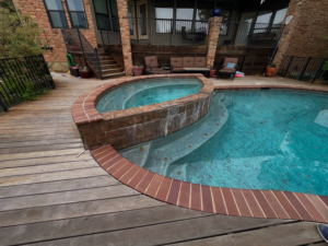 A beautifully finished pool and spa with brick coping and a wooden deck, completed by Austin Pool Plastering in Austin, TX.