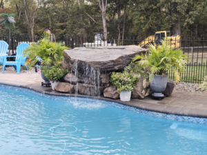 A finished composite pool with a rock waterfall feature, with an excavator visible, by Composite Pools USA in Newfield, NJ.
