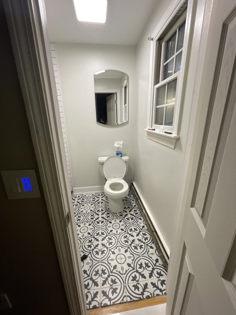 A completed powder room featuring stylish patterned floor tiles and a new toilet, renovated by Granite State Handyman & Home Repair in Derry, NH.
