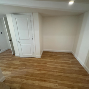 A newly finished room with new flooring, white walls, and a white door installed by Markos Construction in Cambridge, MA.