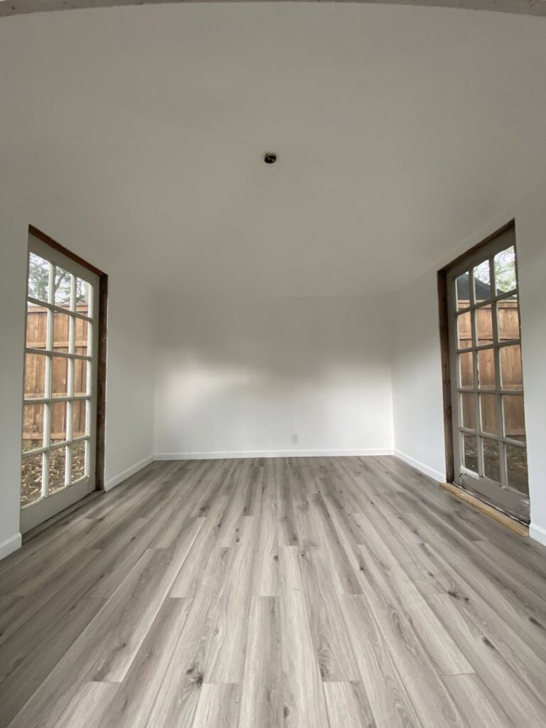 A newly remodeled room with fresh paint and modern laminate flooring installed by Elite Handyman & Remodeling in Dallas, TX.