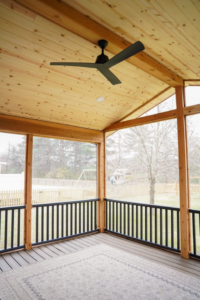 The interior of a finished screened porch featuring a ceiling fan by Vision Construction in Framingham, MA.